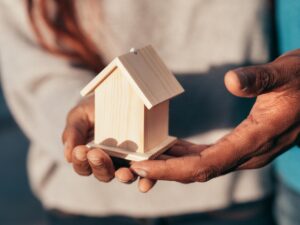Home Close-up of hands holding a small wooden house, symbolizing real estate or home ownership.